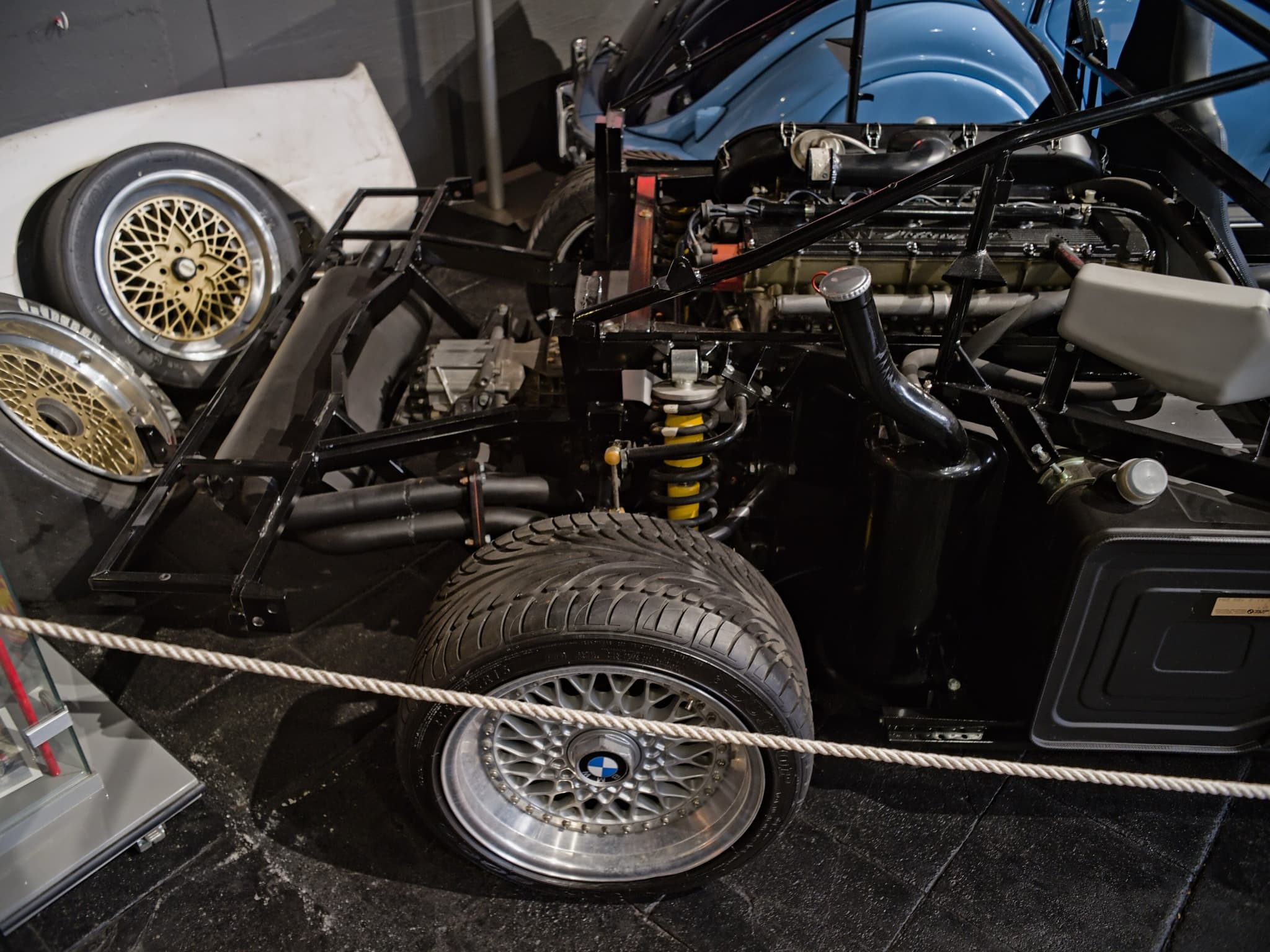 A BMW M1 shown without its body panels: the black tubular steel frame, the six-cylinder engine, a yellow coil-over damper and racing wheels.