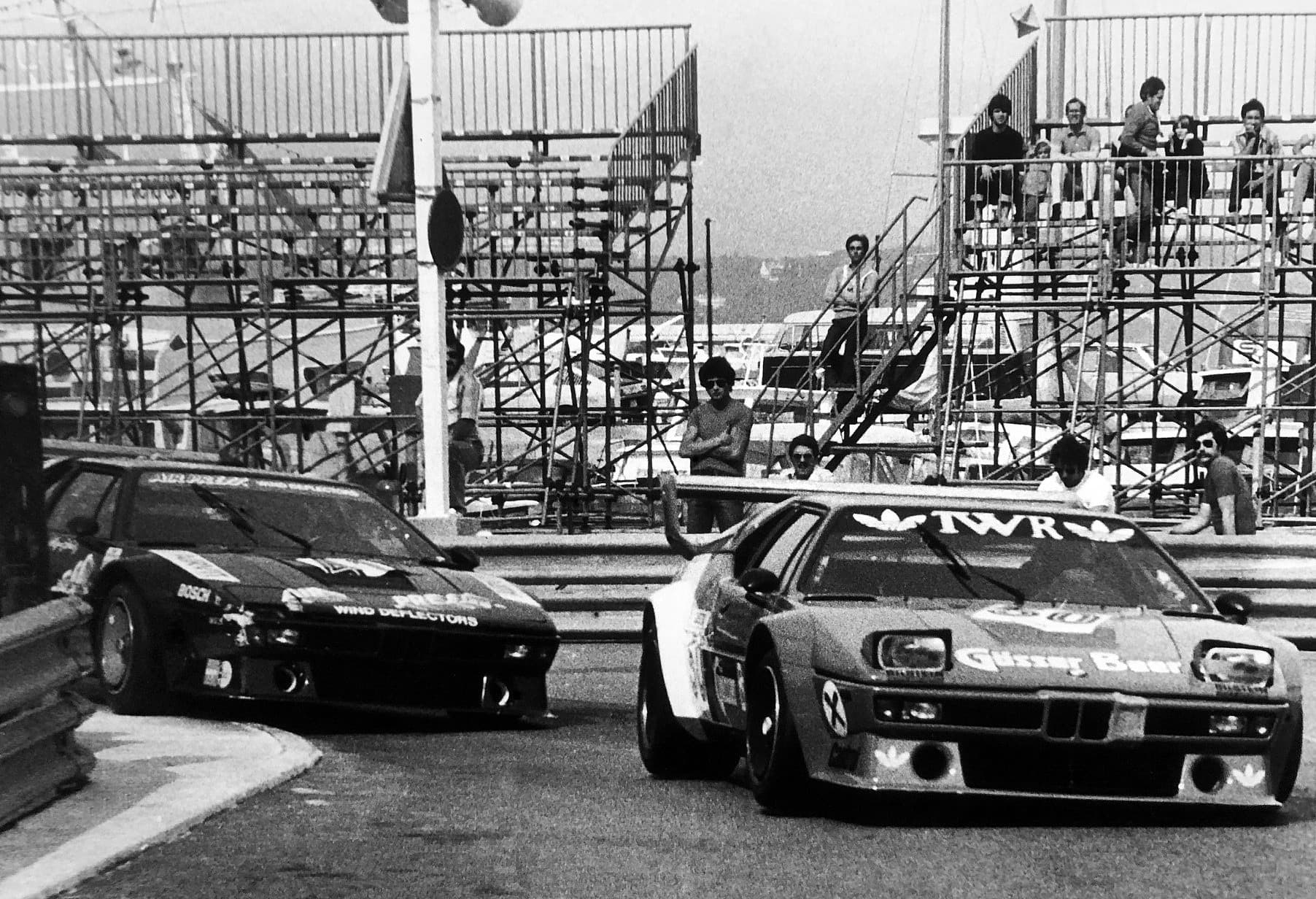 A black and white photograph of two Procars at Monaco, a dark car lettered Airpress Wind Deflectors and a light car lettered TWR and Gösser Beer.