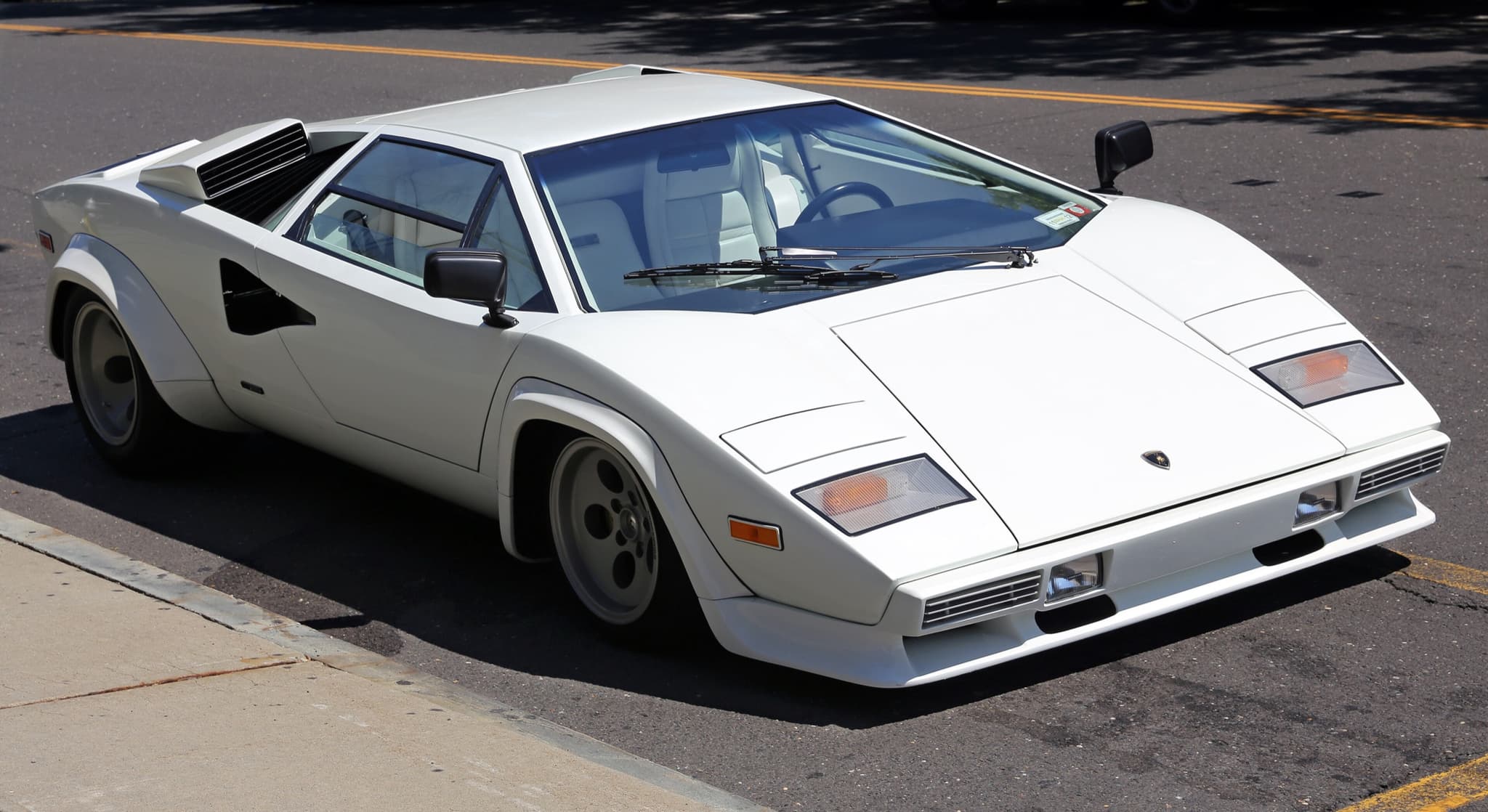 A white Lamborghini Countach LP400 S parked at a kerb in bright sun.