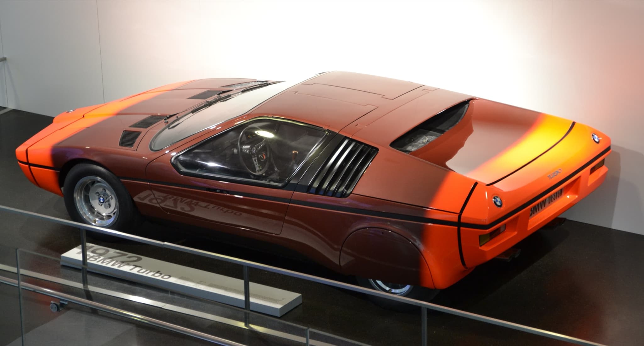 The orange 1972 BMW Turbo show car behind a museum rail, with its side louvres and a plinth label.