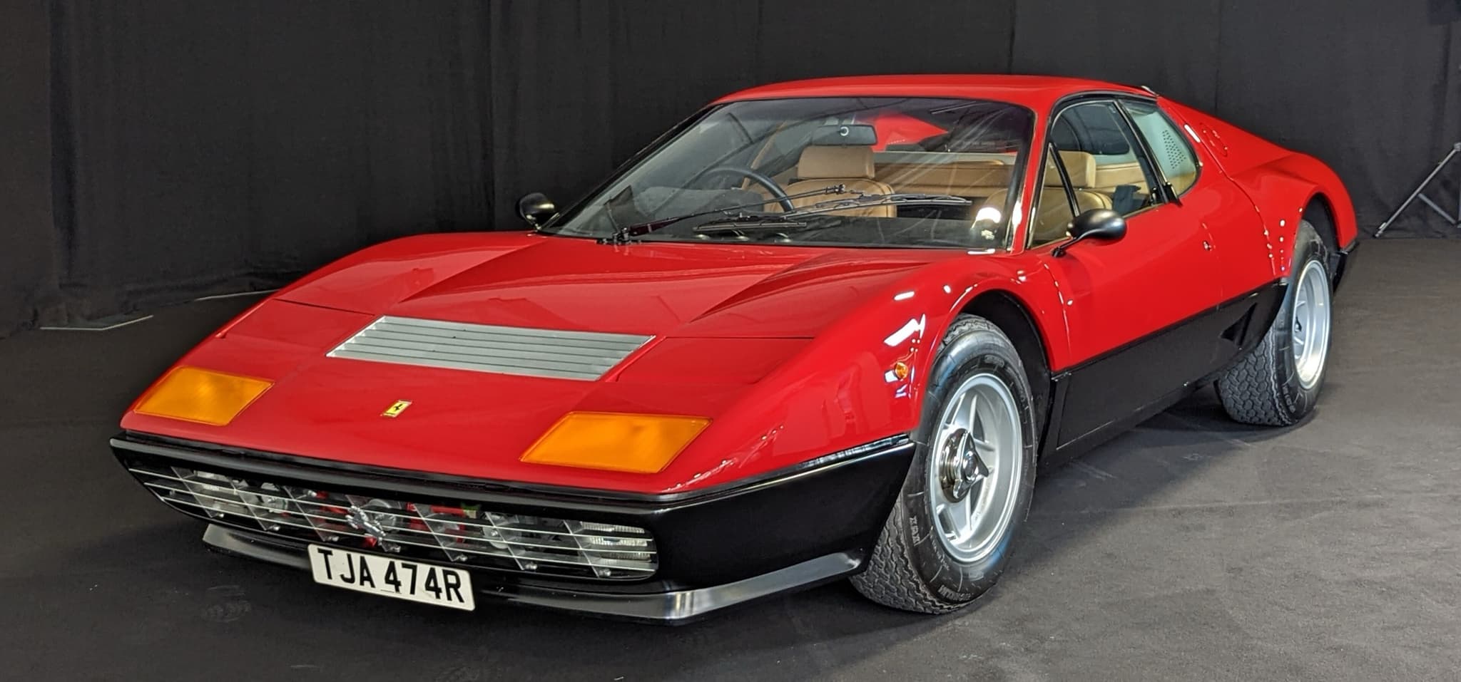 A red and black Ferrari 512 BB on a dark show stand, seen from the front three-quarter.