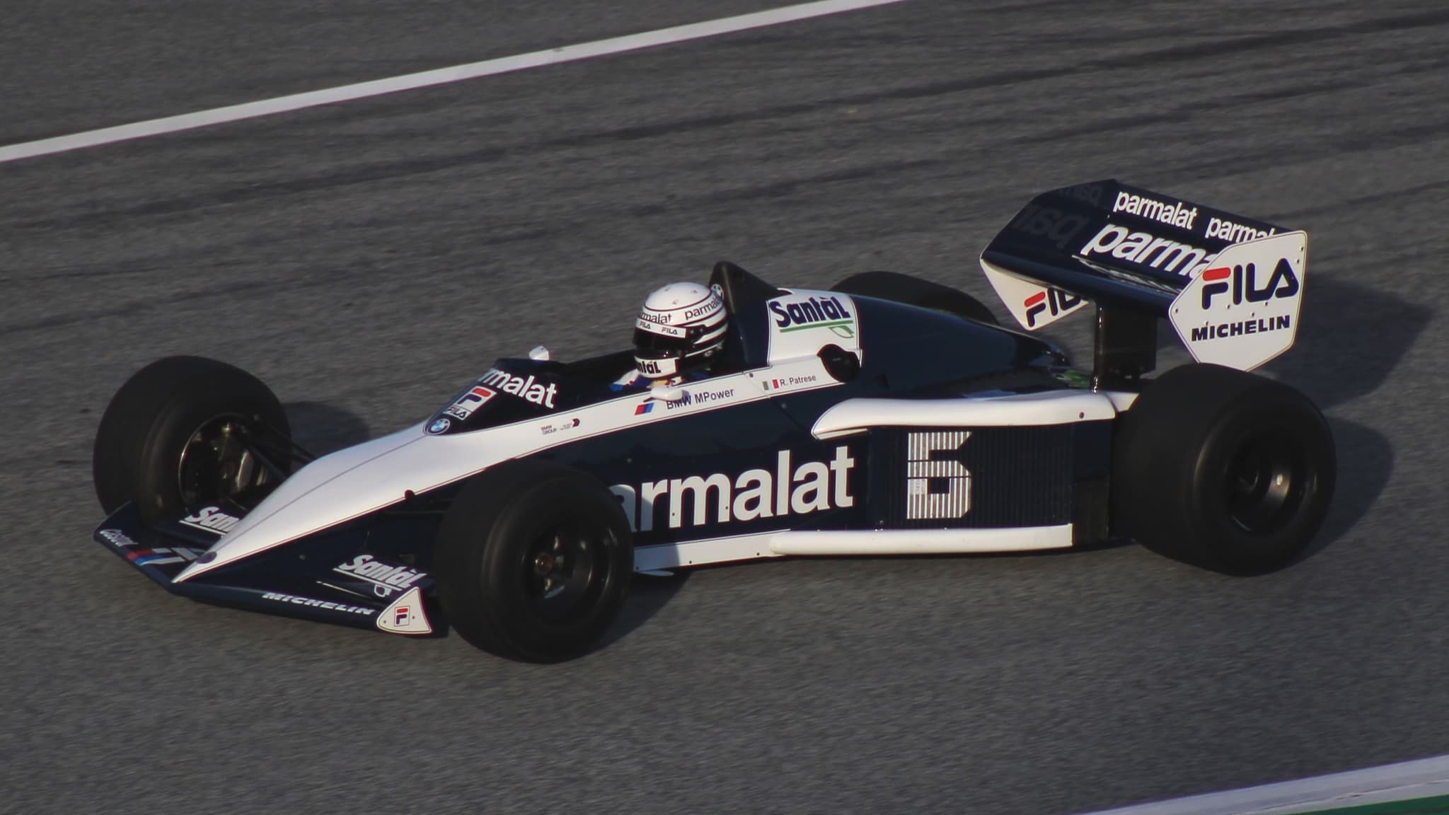 A dark blue and white Brabham BT52 Formula 1 car, number 6, on track in evening light.